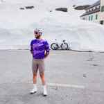 Przemek standing triumphantly at the summit of Passo Gavia, surrounded by towering snow walls in June, capturing the awe-inspiring alpine scenery after a challenging cycling ascent.