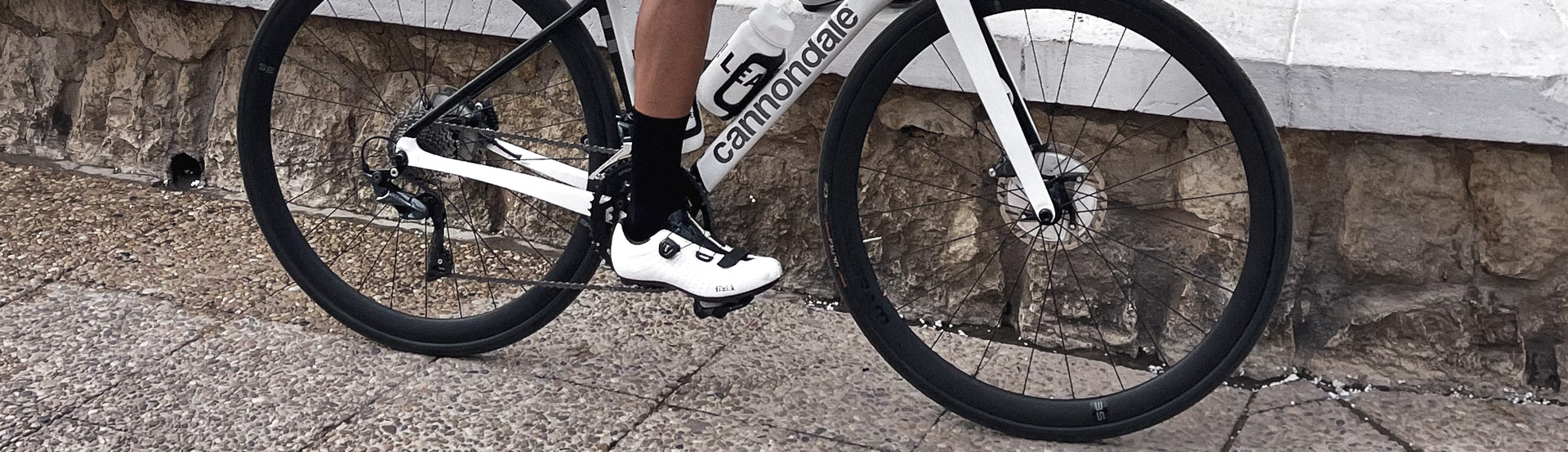 A cyclist wearing a perfectly coordinated cycling kit with black socks and white cycling shoes, showcasing a blend of retro charm and modern style.